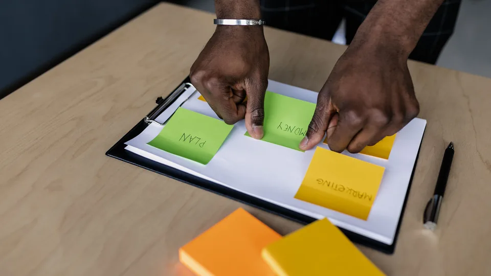 Hands grouping colourful sticky notes on a clipboard for content planning