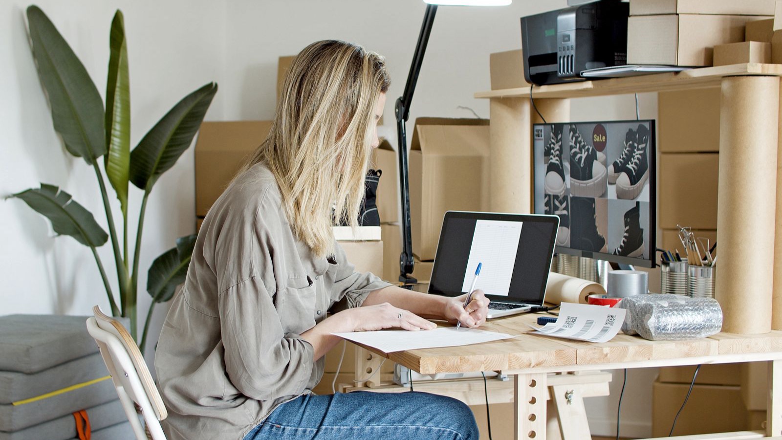 Seller working on a laptop beside product packages and a clothing rack