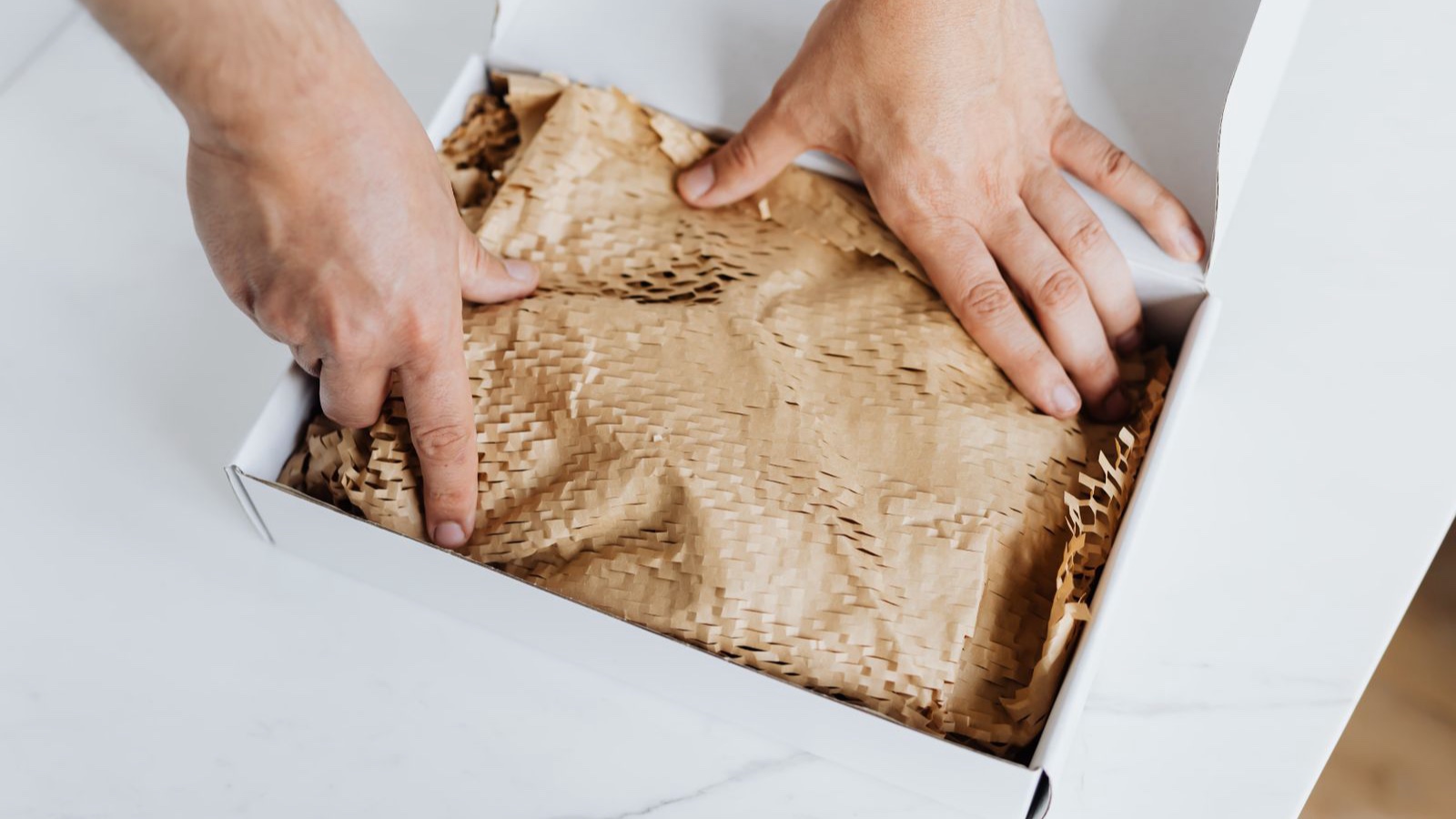 Hands placing protective paper inside a shipping box