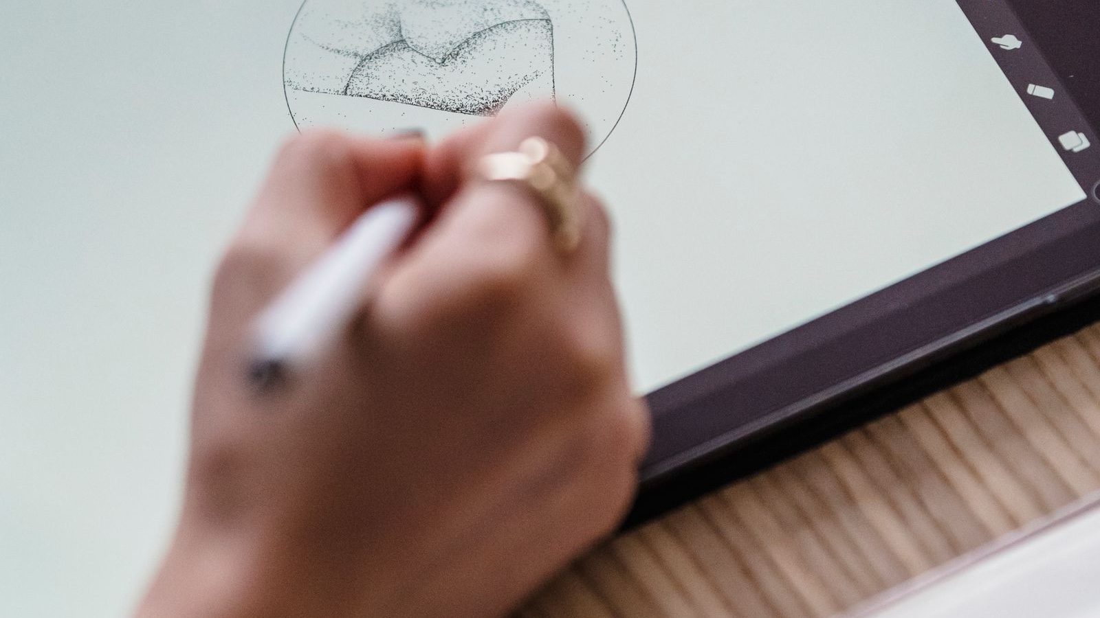 Logo design brief: What should you tell your designer? A close-up of an artist's hand sketching on a digital tablet in a creative workspace.