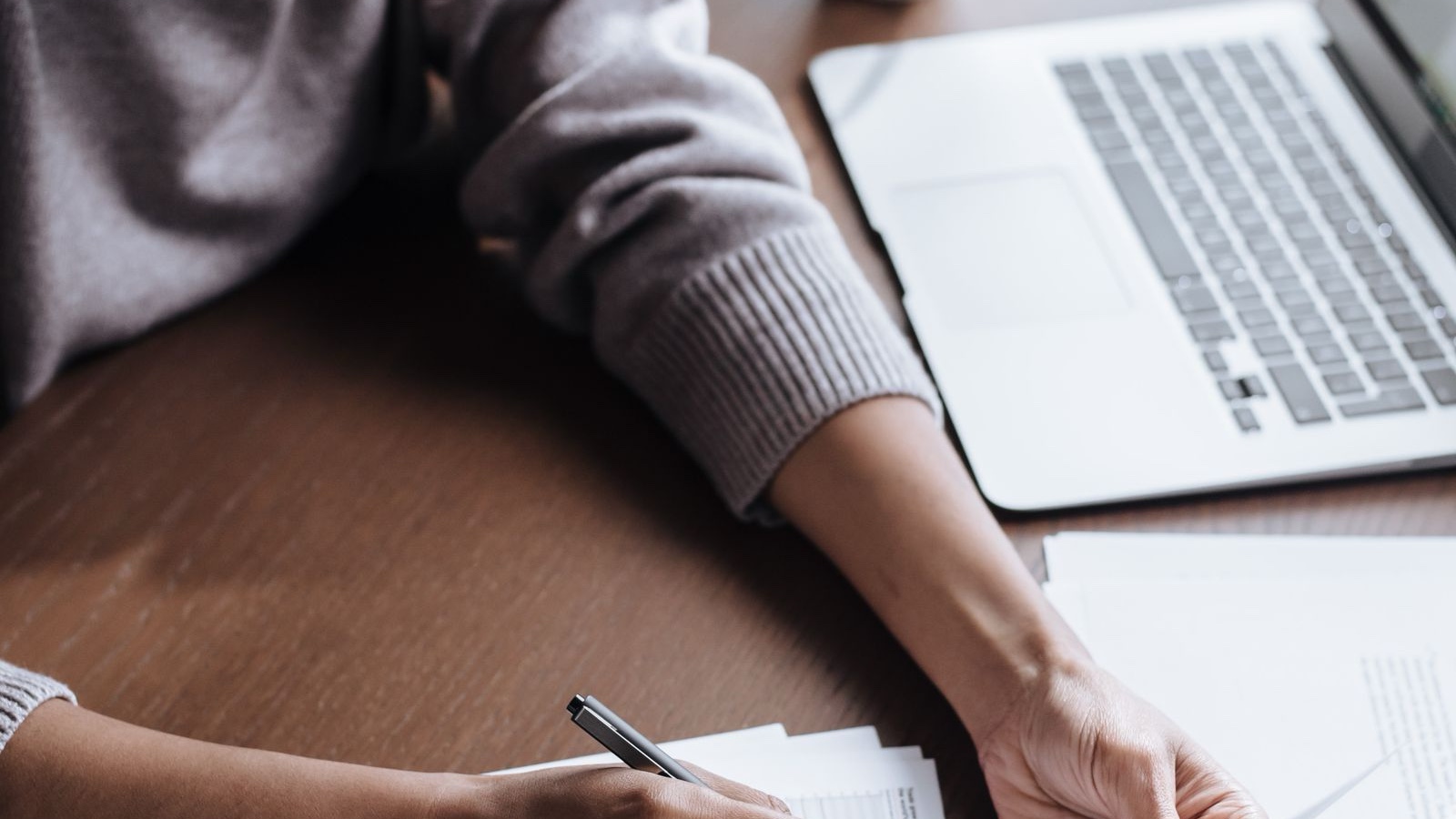 A woman reviewing documents and taking notes beside a laptop