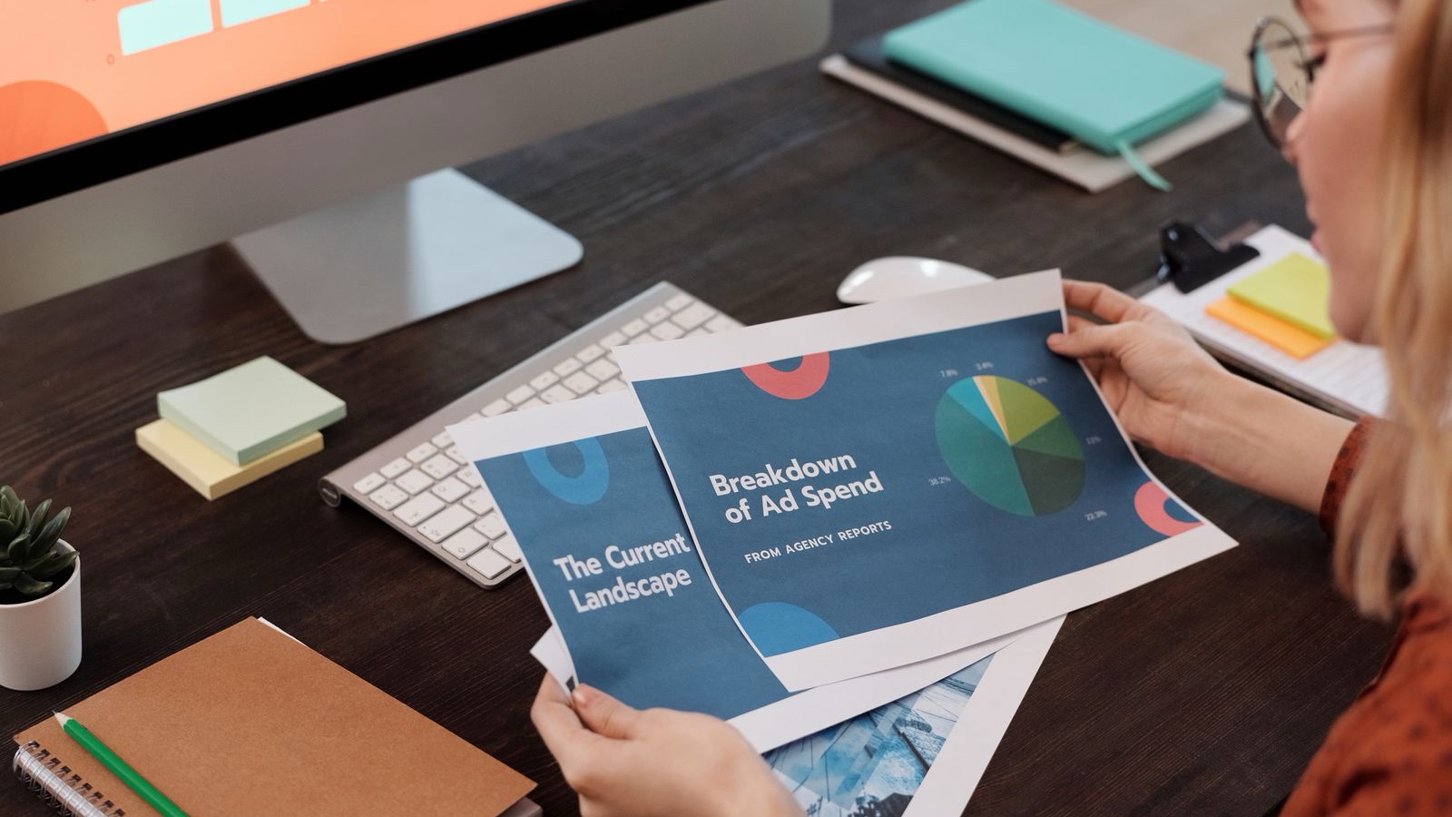 A person reviewing printed graphic design examples beside a laptop