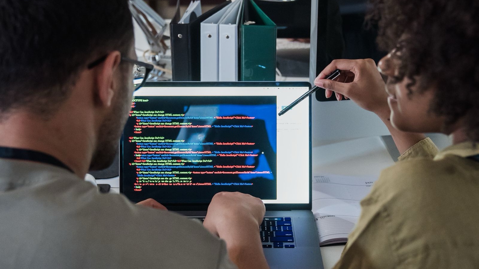 Two developers engage in software programming on a laptop in a modern office setting.