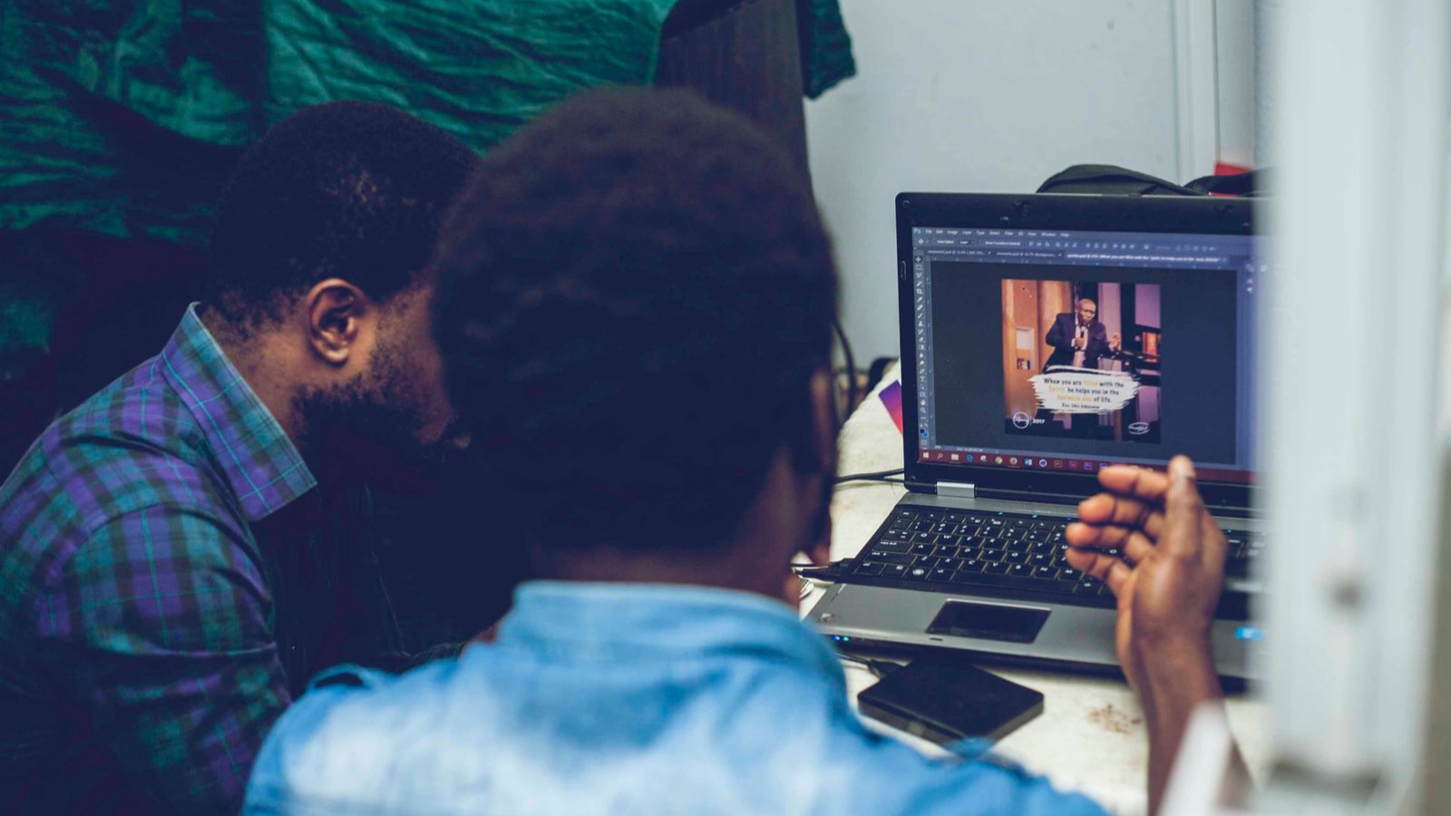 Two men collaborating on graphic design using a laptop indoors, focusing on technology and teamwork.